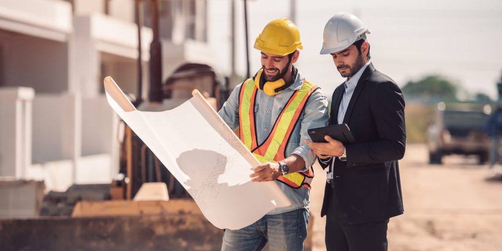Civil engineer and construction worker manager holding digital tablet and blueprints , talking and planing about construction site.  Cooperation teamwork concept.